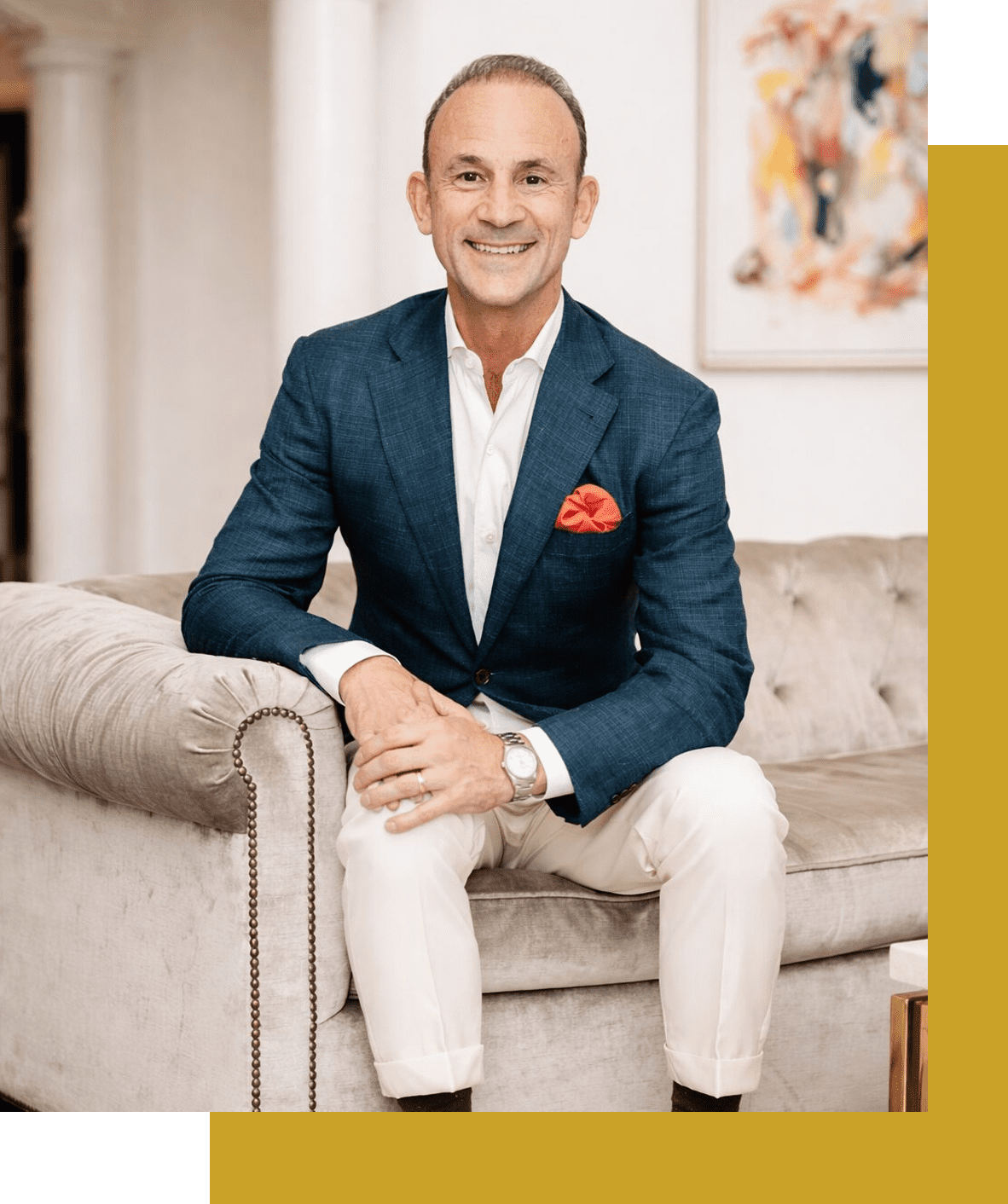 Man in a blue blazer sitting on a beige sofa, smiling.