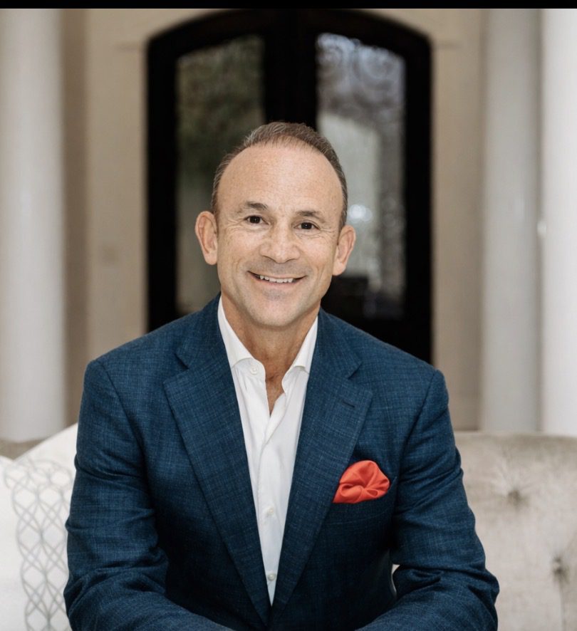 Smiling man in a blue suit sitting indoors.