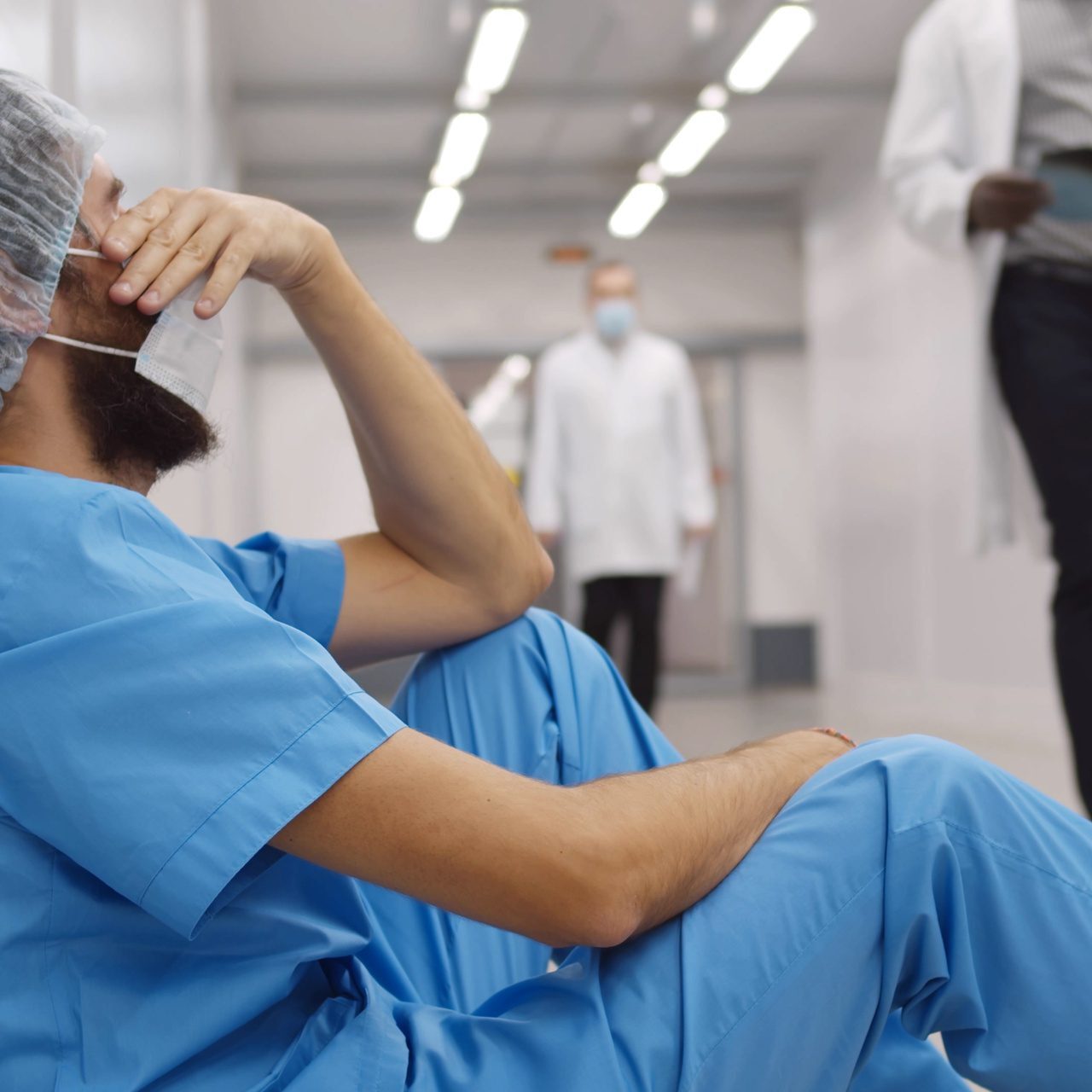 Tired healthcare worker sitting on hospital floor, reflecting.