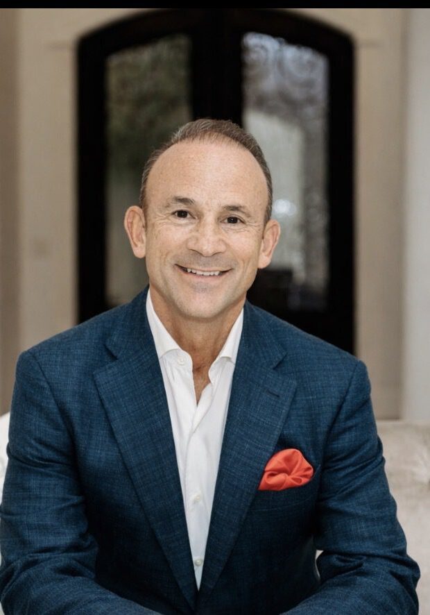 Smiling man in a blue suit sitting indoors.