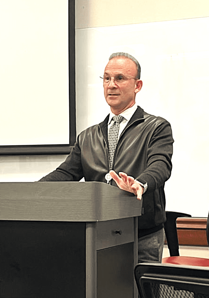 A man giving a lecture at a podium in a classroom.